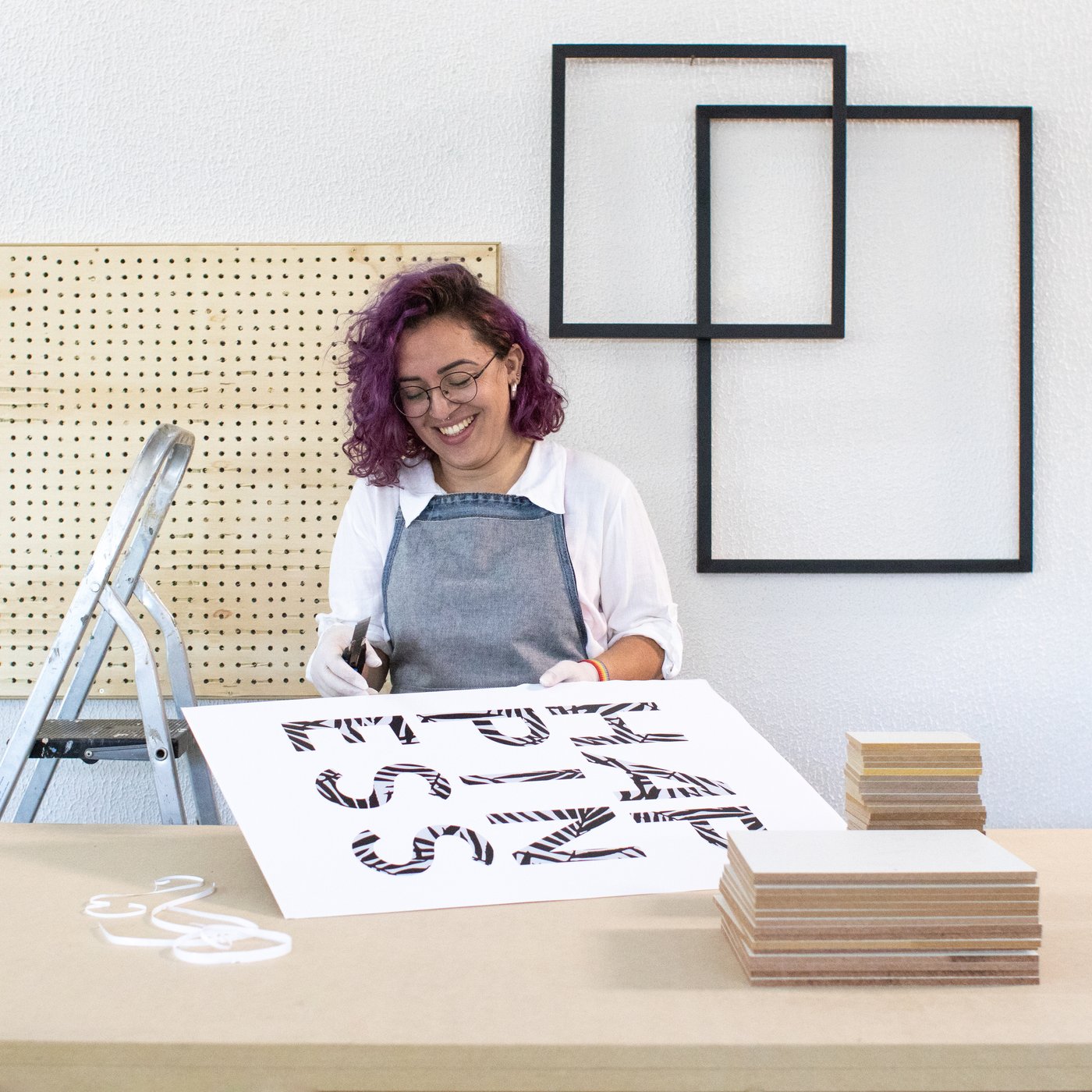 Artista sorrindo na oficina, aplicando letras em um pôster